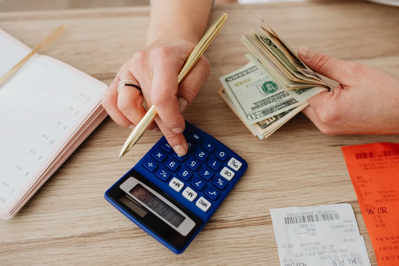 Hands counting dollar bills beside a calculator and notebook