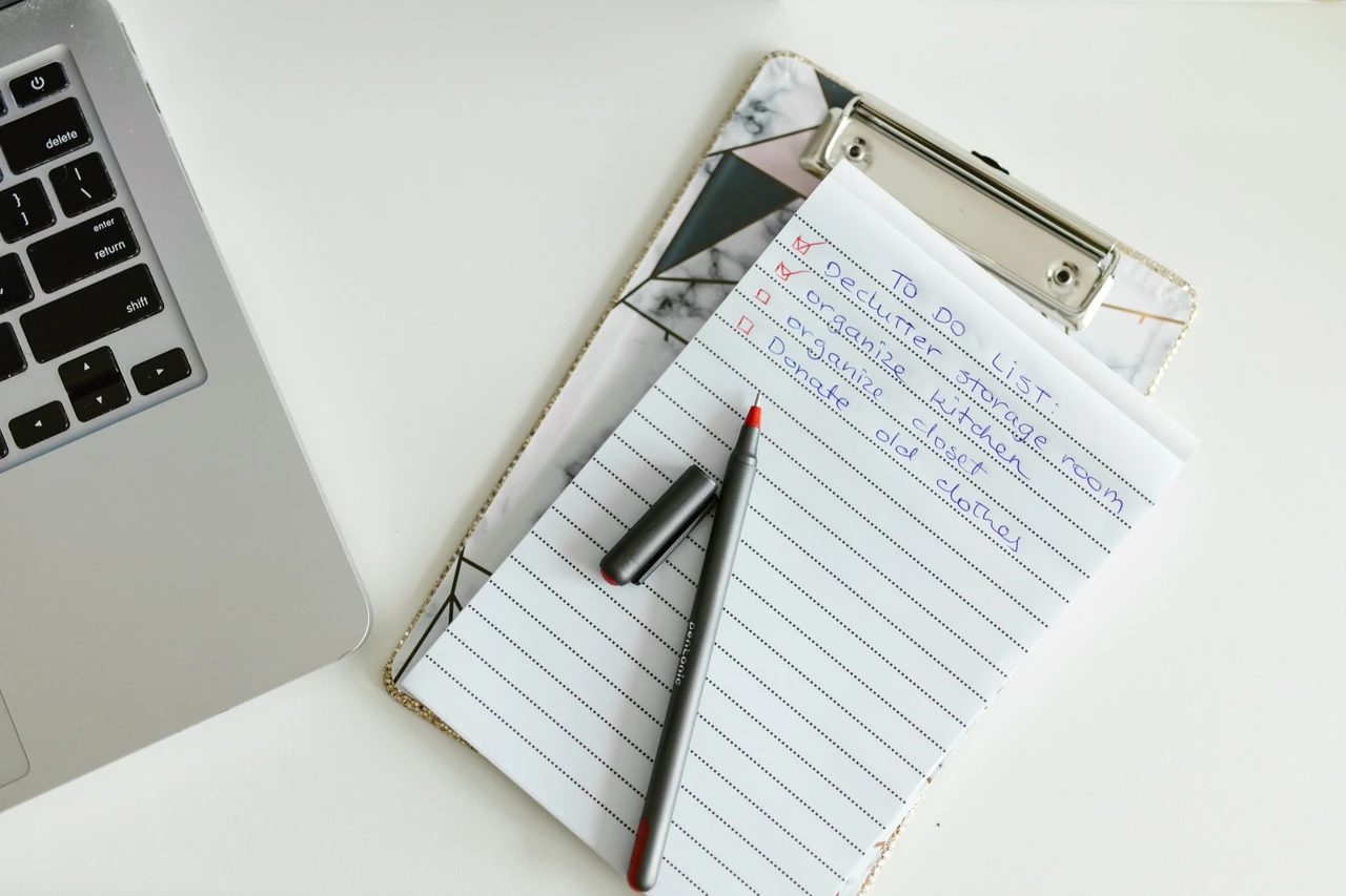 Clipboard with a lined notepad and pen beside a laptop