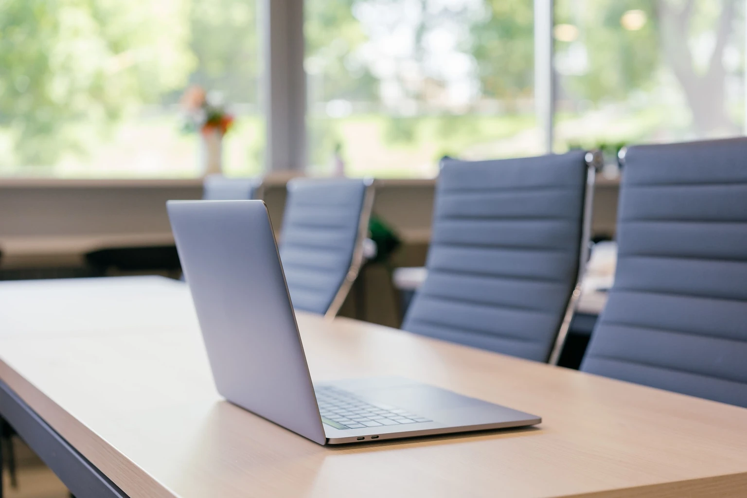 Laptop on a meeting table with blue chairs near a window