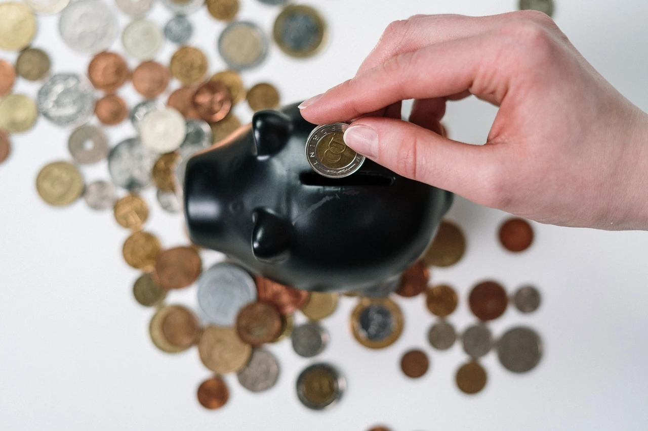 Hand dropping a coin into a black piggy bank