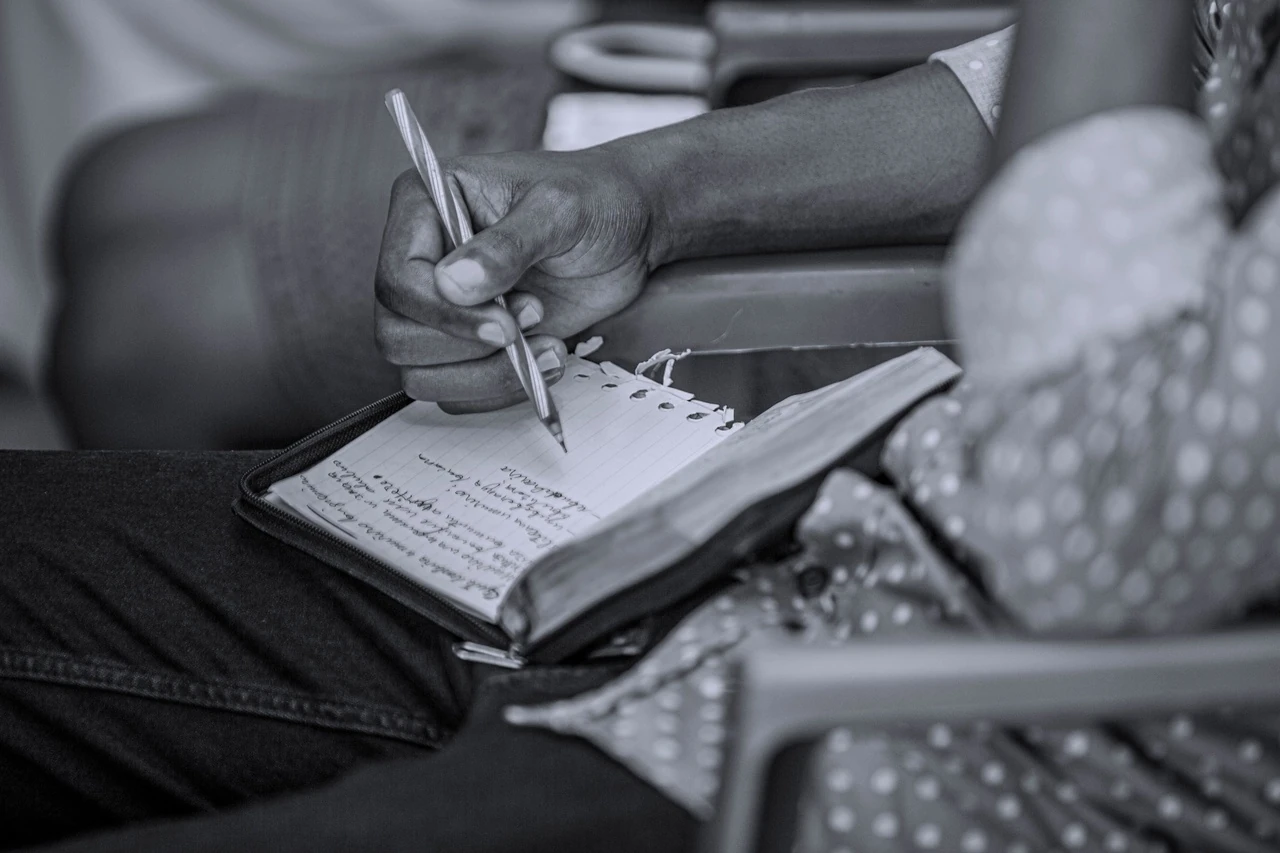 Black and white photo of hands writing in a small notebook