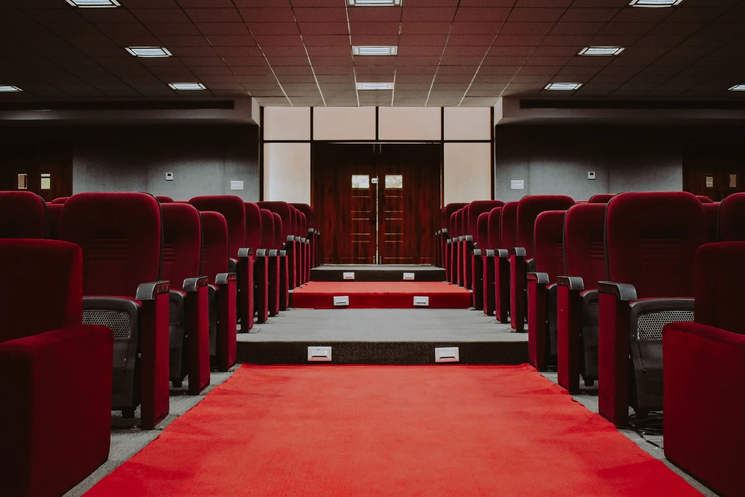 Formal meeting hall with red chairs and a center aisle